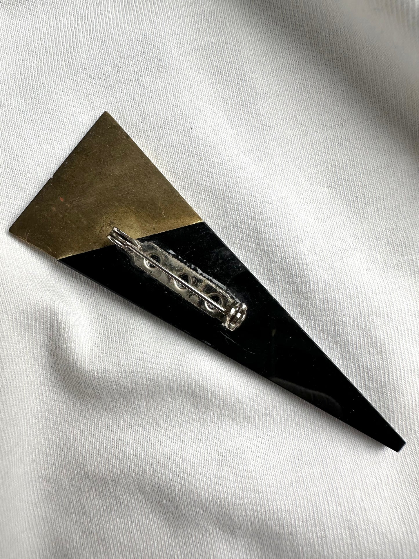 Achterkant van zwarte vintage broche in driehoek met messing rand