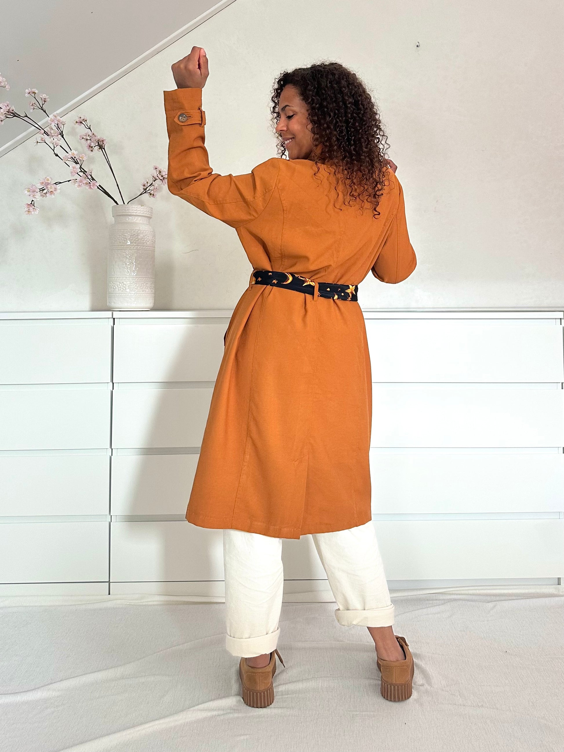 Achteraanzicht van vintage trenchcoat in karamelkleur met ceintuurdetail.