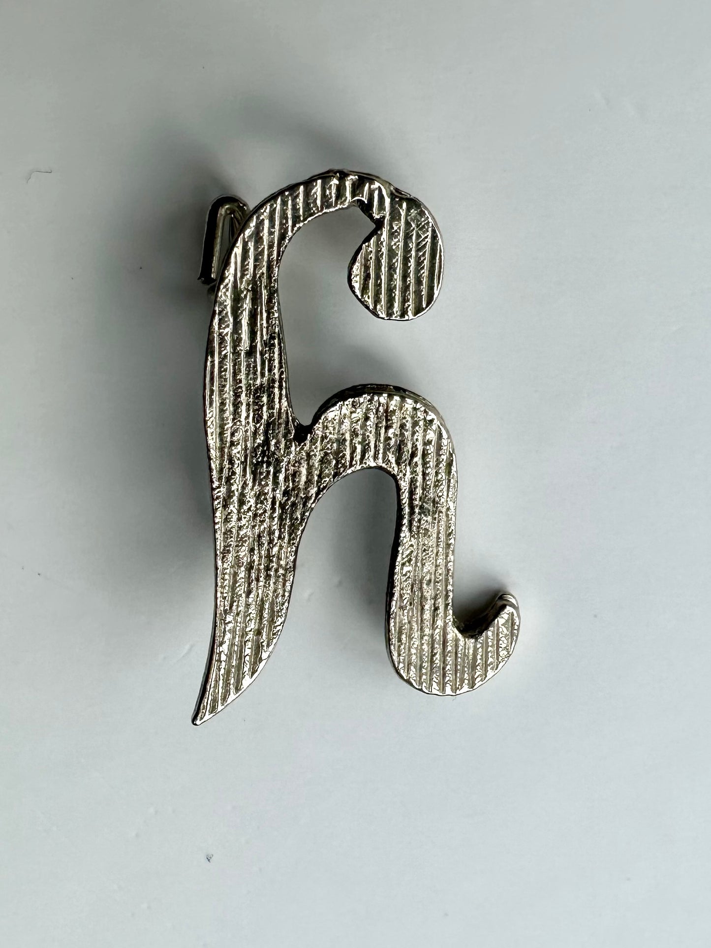 Zilverkleurige vintage broche in de vorm van een sierlijke letter H