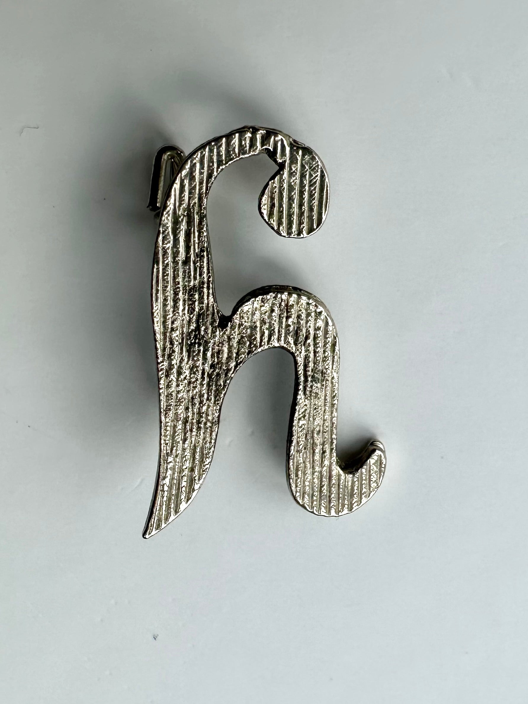 Zilverkleurige vintage broche in de vorm van een sierlijke letter H