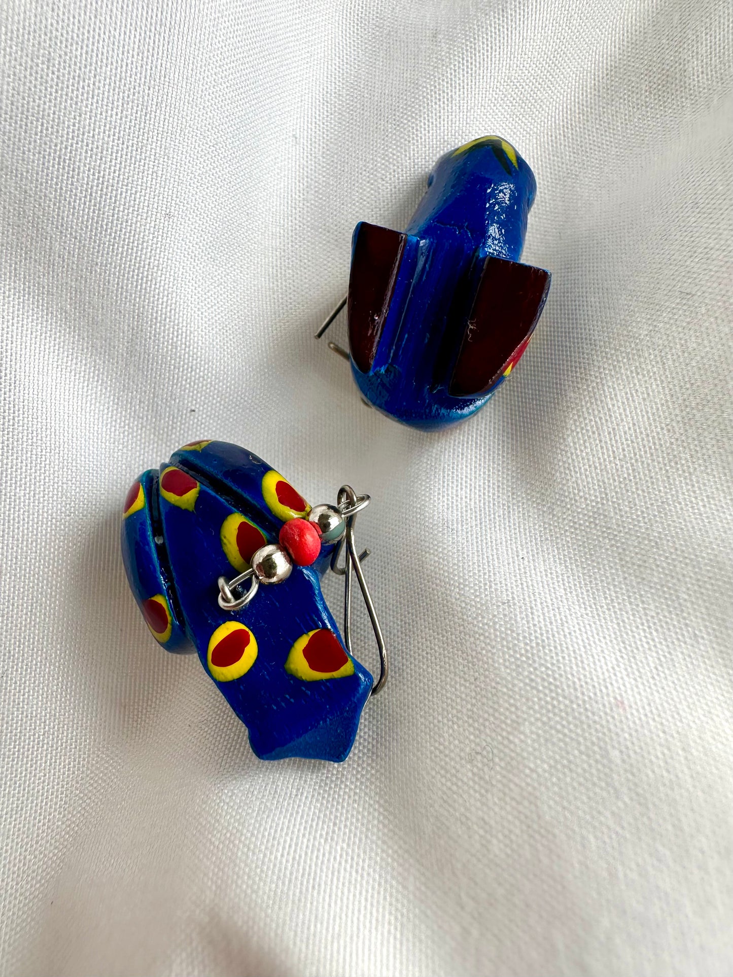 Bovenaanzicht van houten kikker oorbellen in felblauw, handbeschilderd met gele en rode stippen