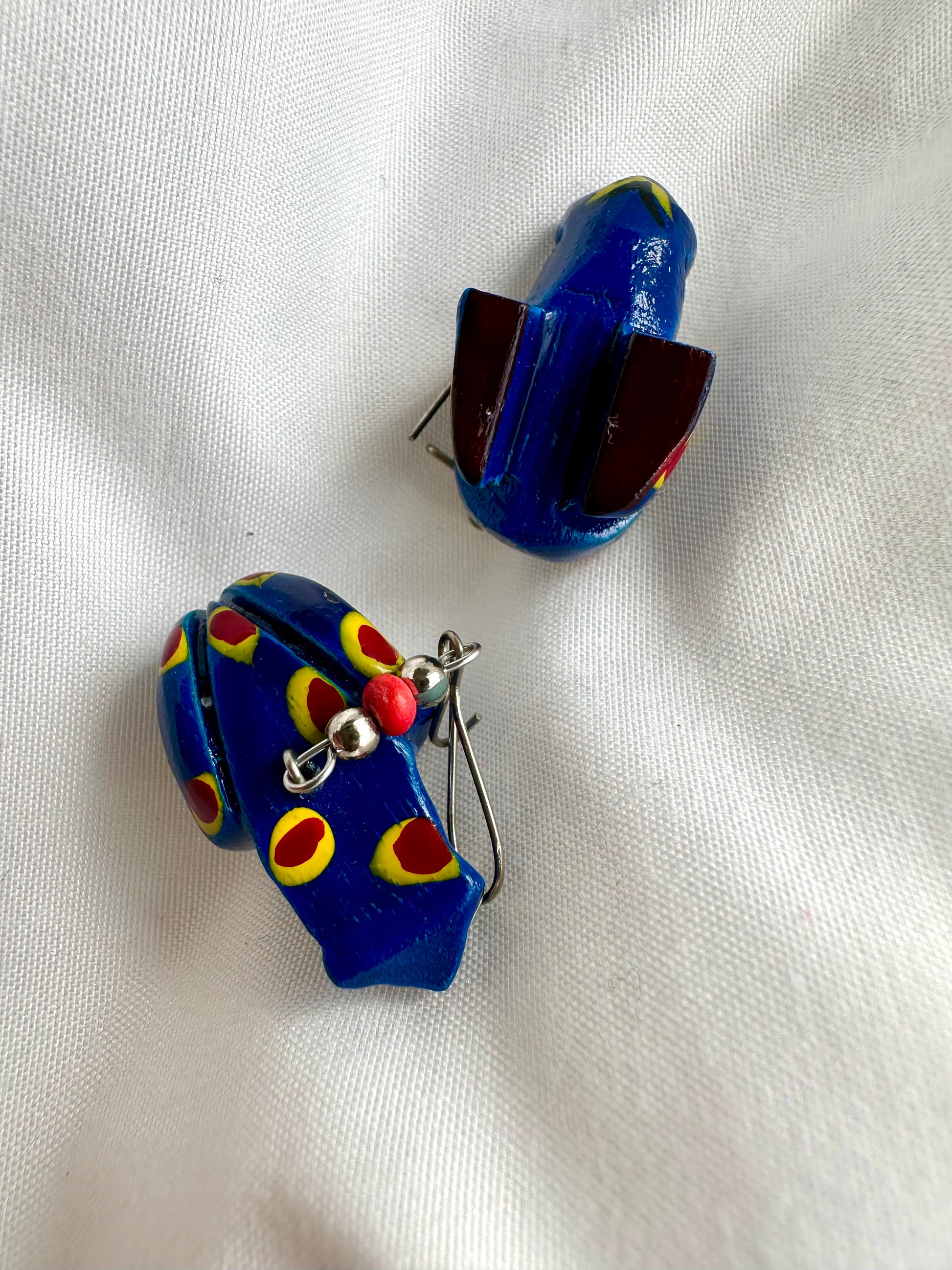 Bovenaanzicht van houten kikker oorbellen in felblauw, handbeschilderd met gele en rode stippen